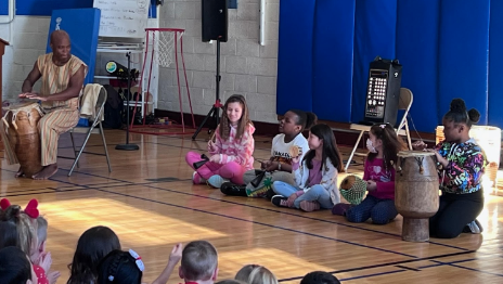 children sitting on gym floor listening to musician